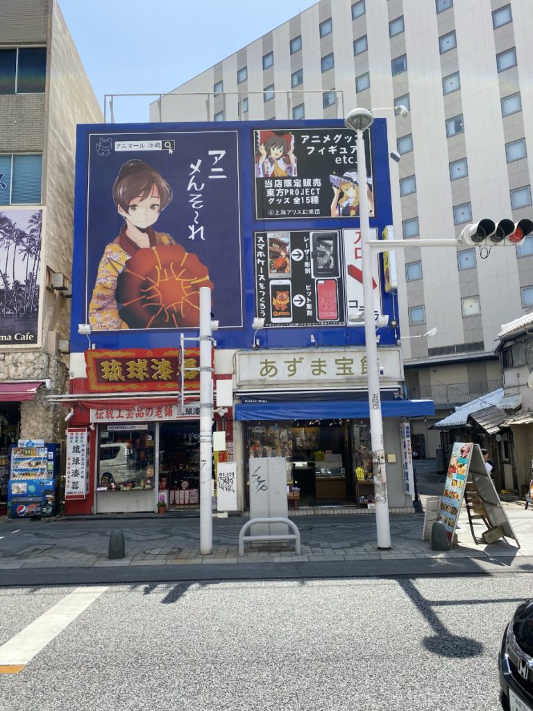 A photo of the Ani-mall Okinawa front sign on Kokasai street in Naha Okinawa. The photo shows a anime style drawing of a lady wearing traditional Ryukyu wear.