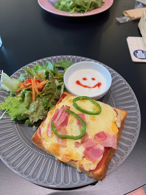 A photo of a pizza toast, salad, and yogurt. The yogurt has a smily face. 